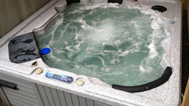 Un jacuzzi con panel de control, pared de madera y revestimiento tipo piedra.