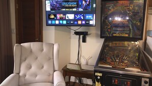 Una habitación con una televisión mostrando un programa, un sillón cómodo y un juego de arcade de una fuerza policial antigua.