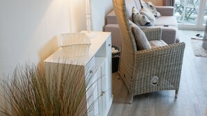 Una sala de estar con una silla de mimbre, un aparador blanco, una lámpara y una planta en maceta.