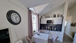 Una cocina moderna con armarios blancos, microondas y cafetera. Hay una mesa de comedor con sillas y un reloj en la pared.