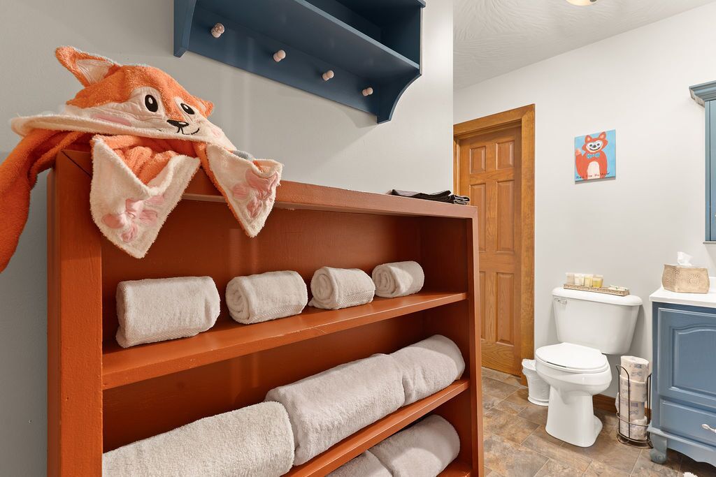Une salle de bain avec une étagère en bois où sont rangées des serviettes, des toilettes et un meuble bleu.