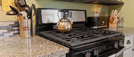 A kitchen with a gas stove, a kettle, and various utensils in a holder.