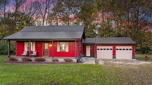 A red building with a garage, a porch with two chairs, and a small staircase leading to the entrance. - Red Fox Hollow - Hocking Hills, Clear Creek, Hot Tub, Fire Pit and Swing (AMANDA)