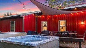 A hot tub on a wooden deck with a red exterior wall, a covered patio area, and string lights. - Red Fox Hollow - Hocking Hills, Clear Creek, Hot Tub, Fire Pit and Swing (AMANDA)