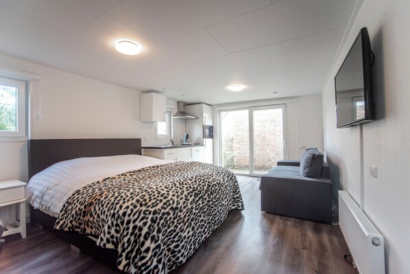 A bedroom with a bed, a desk, a TV, and a window.