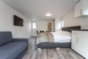 A modern bedroom with a bed, a sofa, and a TV mounted on the wall.