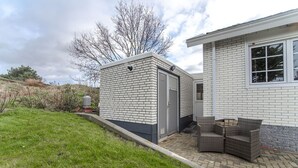 Et moderne hus med murstensfacade, en overdækket terrasse med fletningsmøbler og en klar himmel.