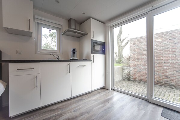A modern kitchen with white cabinets, a black countertop, a built-in microwave, and a window overlooking a brick wall.