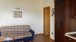 Uma sala de estar com sofá quadriculado, vigas de madeira no teto, um armário e uma porta que dá para outro cômodo.