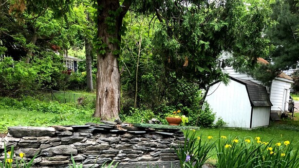 A garden with a stone wall, various plants, and a small shed. - Gardner Farm Inn (Troy)