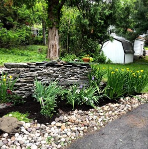 A garden with a stone wall, various plants, and a small shed. - Gardner Farm Inn (Troy)