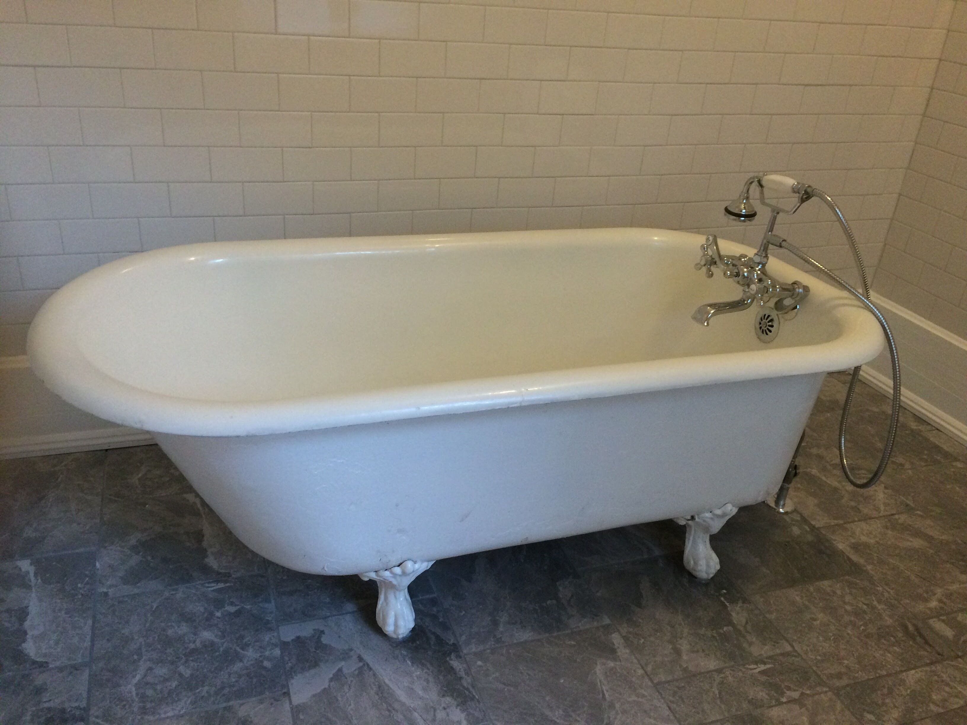 Una bañera blanca independiente con patas de garra, cabezal de ducha de mano y tapón de desagüe.