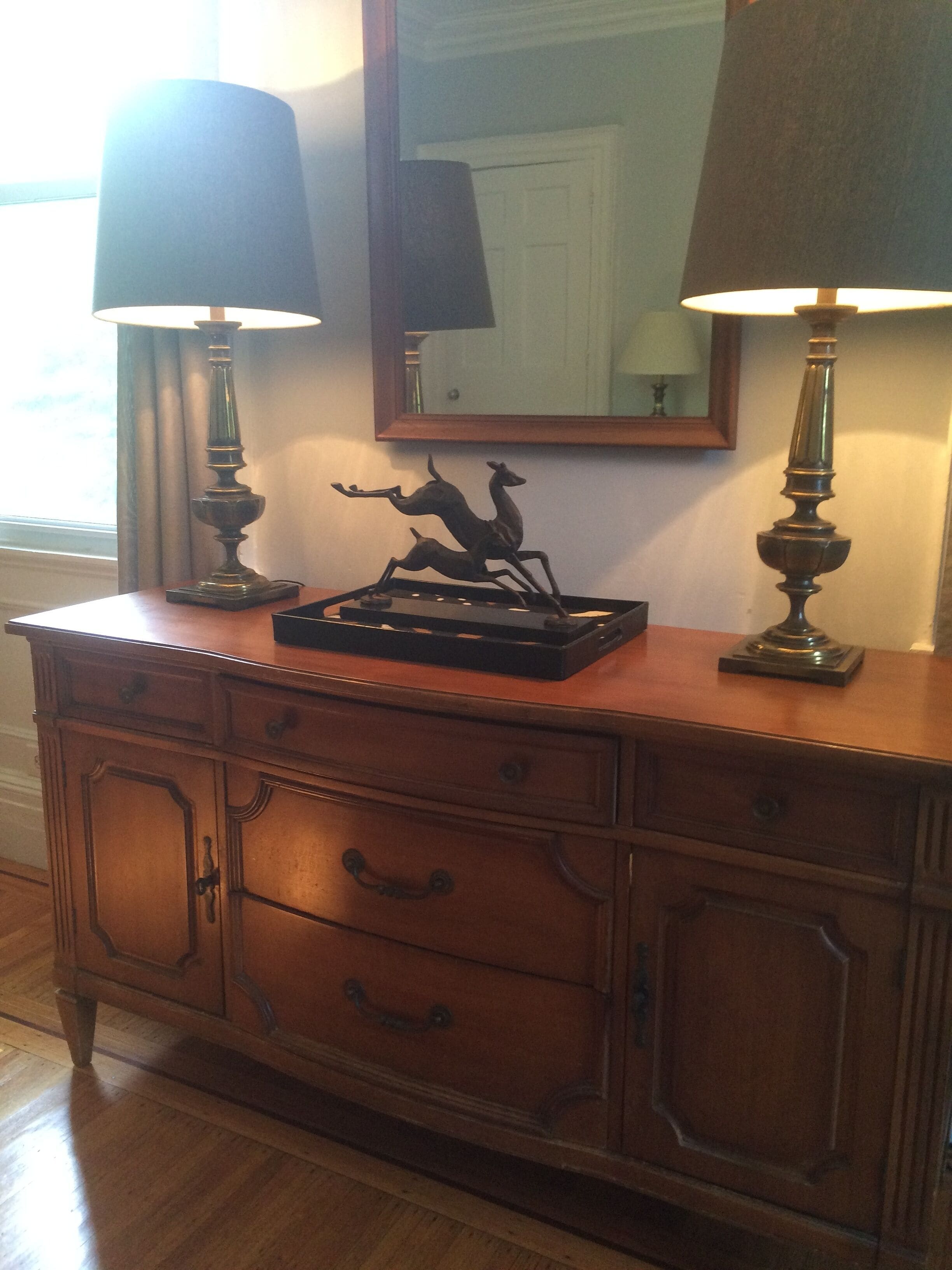 A wooden dresser with two lamps, a mirror, and a sculpture of deer.