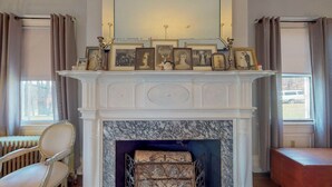 A room with a white fireplace, framed photographs on the mantel, a radiator, and a chair. - Gardner Farm Inn (Troy)