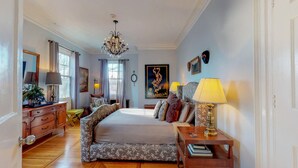 A bedroom with a large bed, a chandelier, a dresser, and a nightstand with a lamp. - Gardner Farm Inn (Troy)