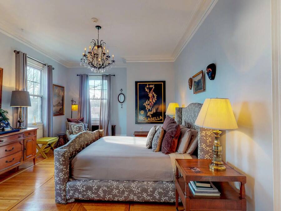 A bedroom with a large bed, a chandelier, a dresser, and a nightstand with a lamp.