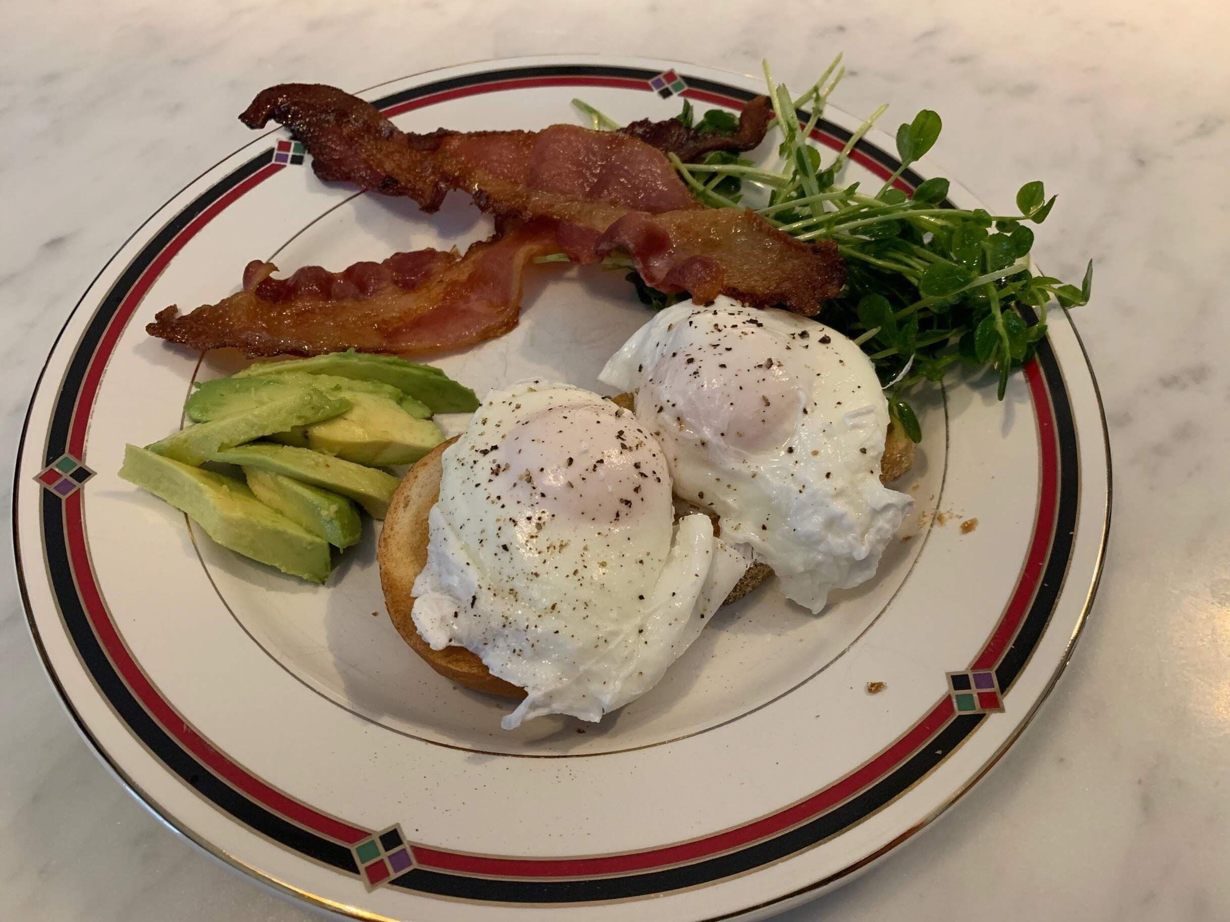 A plate with a breakfast consisting of eggs, bacon, avocado, and greens.