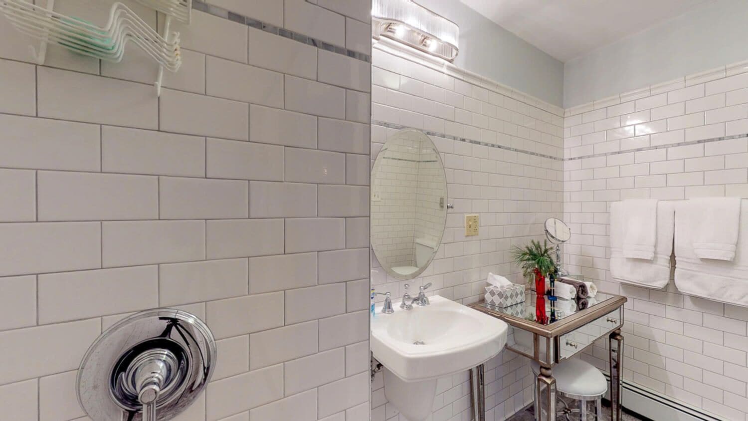 A bathroom with white tiled walls, a sink, a mirror, and a towel rack.
