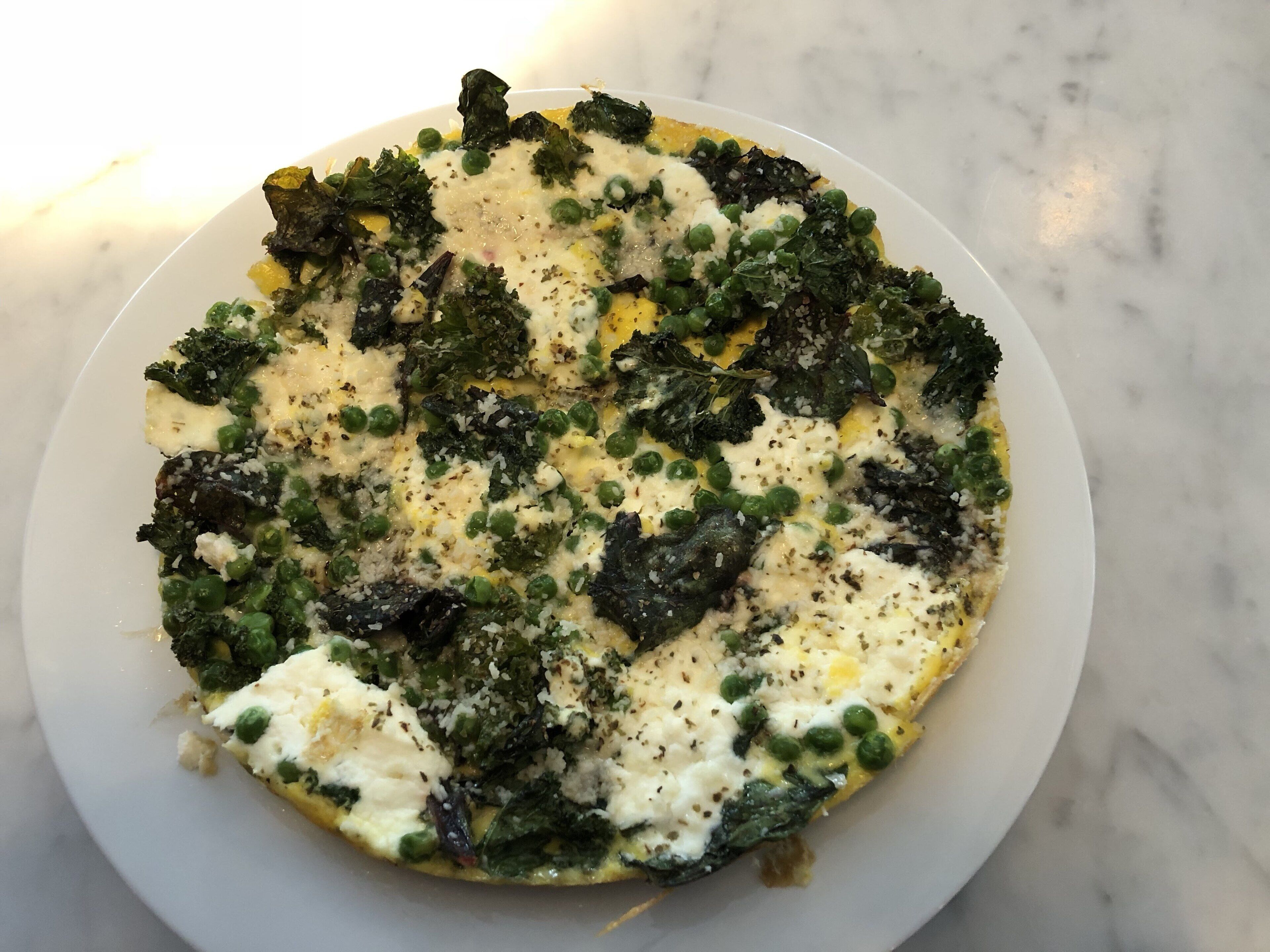 A white plate with a dish containing greens, peas, and cheese.