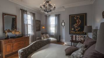 A bedroom with a large bed, a dresser, a chair, a chandelier, and a painting on the wall.