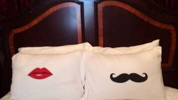 A bed with a wooden headboard and two pillows, one with a red lips design and the other with a black mustache design.