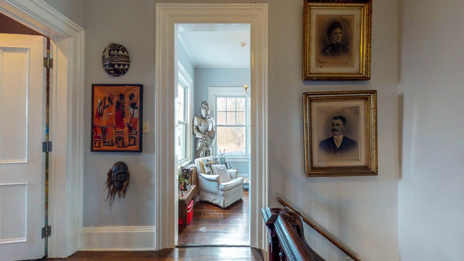 A hallway with a white door, a framed portrait, and a statue.