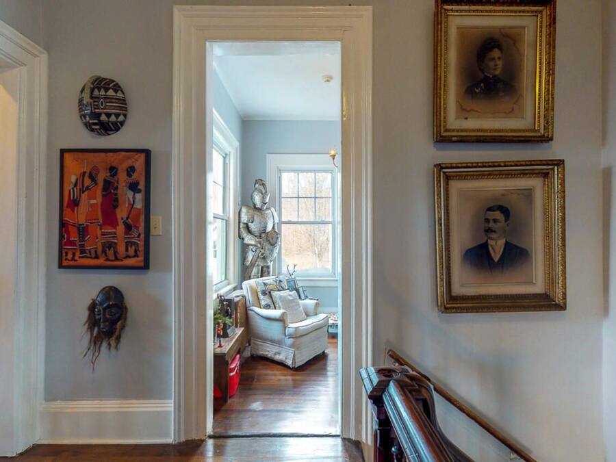 A hallway with a white door, a framed portrait, and a statue.