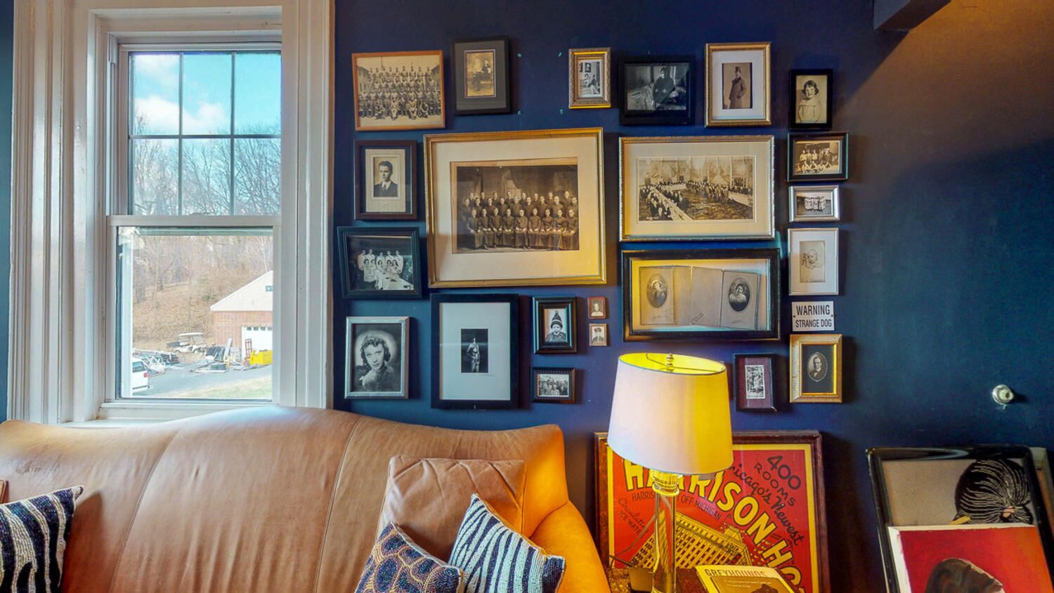 Una habitación con un ventanal grande, un sofá con cojines y una pared decorada con fotografías enmarcadas.