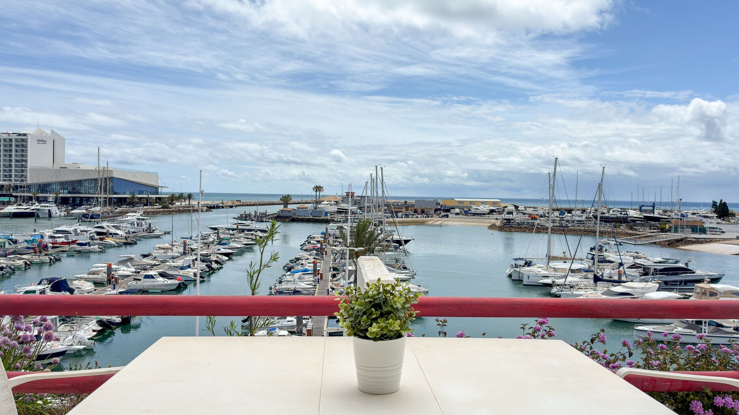 Un port de plaisance où sont amarrés de nombreux bateaux, un bâtiment à l’architecture moderne et un ciel dégagé.