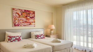 Habitación de hotel con dos camas, un cuadro en la pared, una lámpara y vistas a través de cortinas translúcidas.