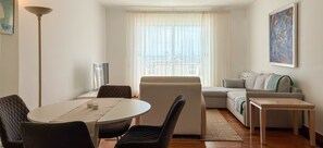 A living room with a sofa, a dining table with chairs, a TV, and a window with curtains.
