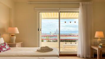 Une chambre d’hôtel avec un lit, deux lampes de chevet, une table avec des livres et une vue sur un port de plaisance, visible à travers une porte-fenêtre coulissante.