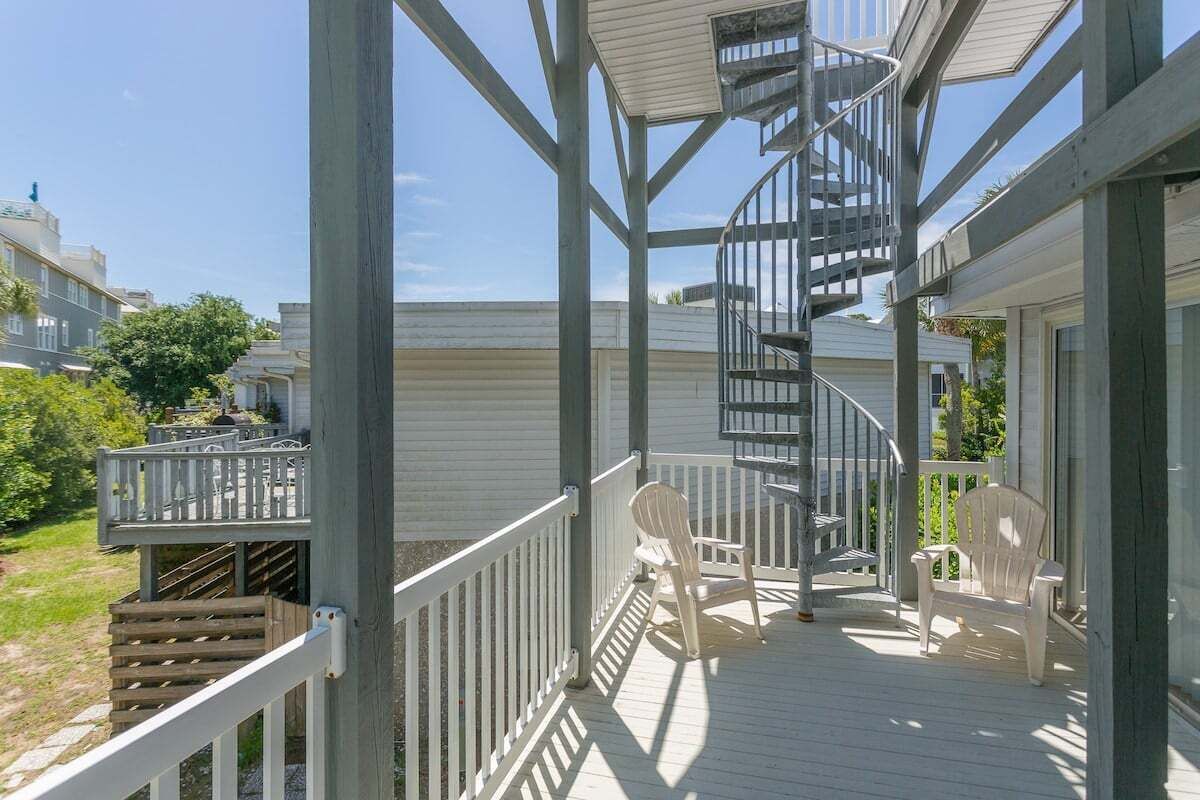 A wooden deck with a spiral staircase, white chairs, and a railing.