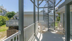 Une terrasse en bois avec un escalier en colimaçon, des chaises blanches et une rambarde.