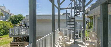 A wooden deck with a spiral staircase, white chairs, and a railing.