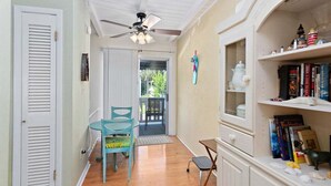 Un couloir avec un ventilateur de plafond, une porte, une fenêtre et une bibliothèque contenant des livres et des objets décoratifs.