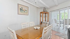 Un coin repas avec une table en bois, des chaises blanches, un lustre et un tableau encadré au mur.