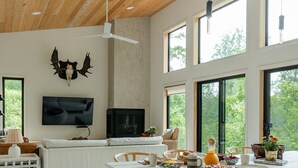 Amplia sala de estar con techo alto, ventanas grandes, chimenea y televisor montado.