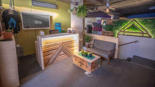 Un espacio de oficina moderno con un mostrador de recepción, un sofá gris y una mesa de centro de madera con plantas.
