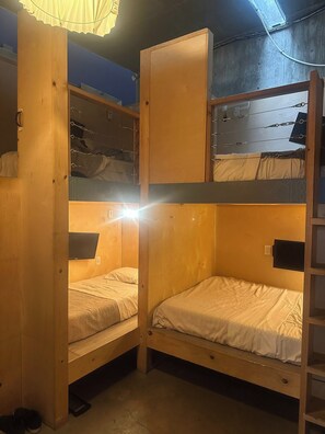 A bunk bed room with a wooden ladder, a TV mounted on the wall, and a window with a curtain. - PodShare San Diego - Hostel (San Diego)