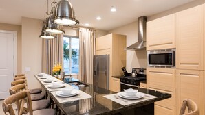 A modern kitchen with a central island, stainless steel appliances, wooden cabinets, and a dining area with chairs and a table set for a meal.