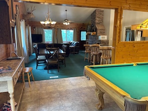 A cozy lodge interior with a pool table, wooden furniture, a stone fireplace, and a dining area.