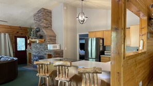 A rustic kitchen with a stone fireplace, wooden bar stools, a stainless steel refrigerator, and a hanging light fixture. - Bryce & Zion midpoint!  Firepit & pool table. ATV trails nearby. (Alton)