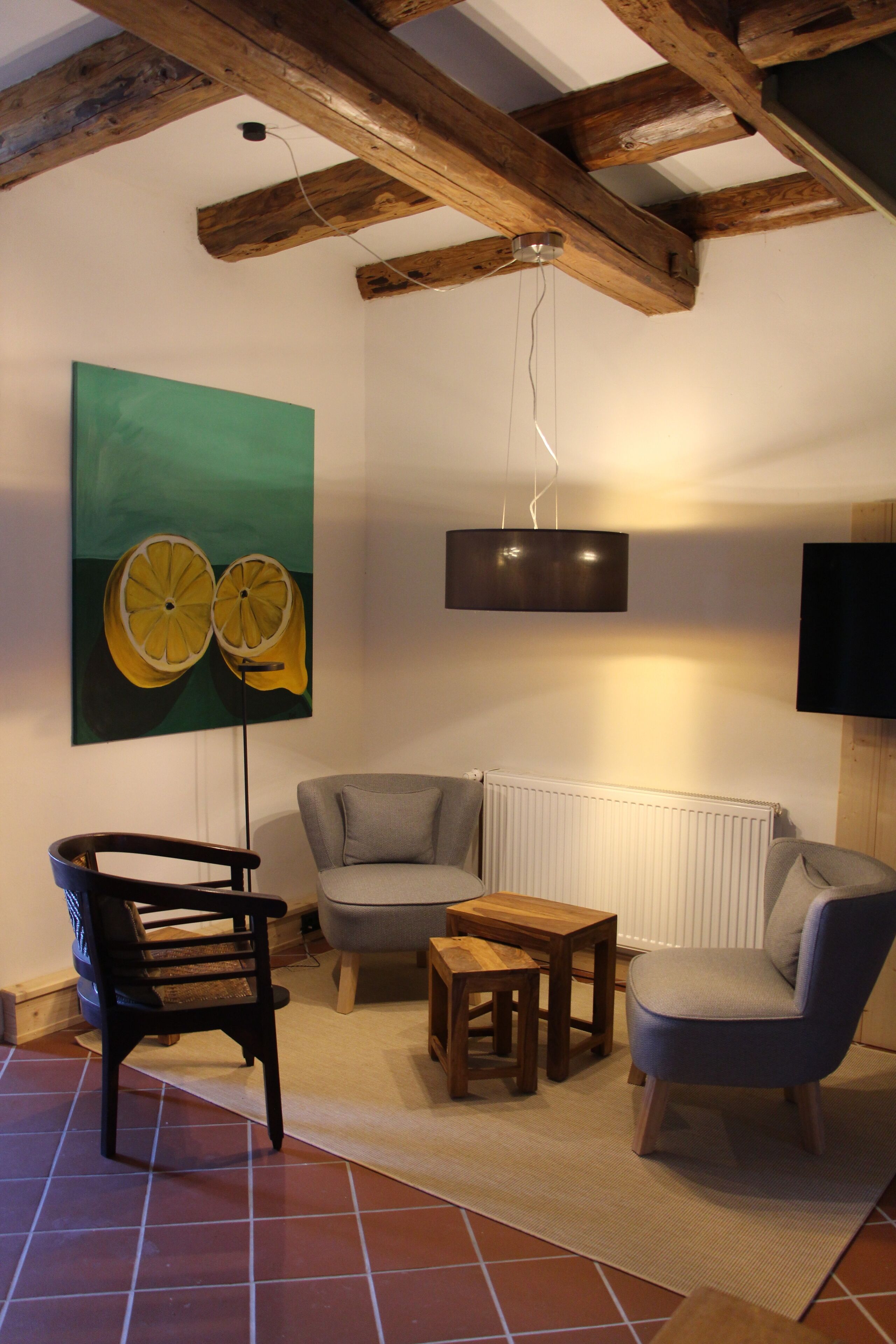 Una sala de estar con techo de madera, una obra de arte verde, un sofá gris, una mesa de madera y una silla negra.