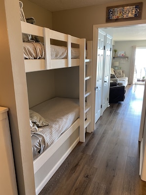 Habitación con literas, suelo de madera, una puerta que da a una sala de estar y un letrero en la pared.