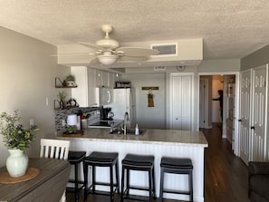 Una cocina moderna con una isla central, taburetes de bar, un ventilador de techo y un reloj en la pared.