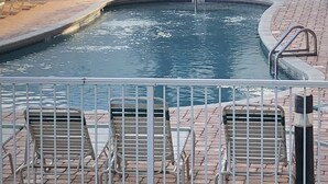 A swimming pool with a tiled deck, lounge chairs, and a gazebo.