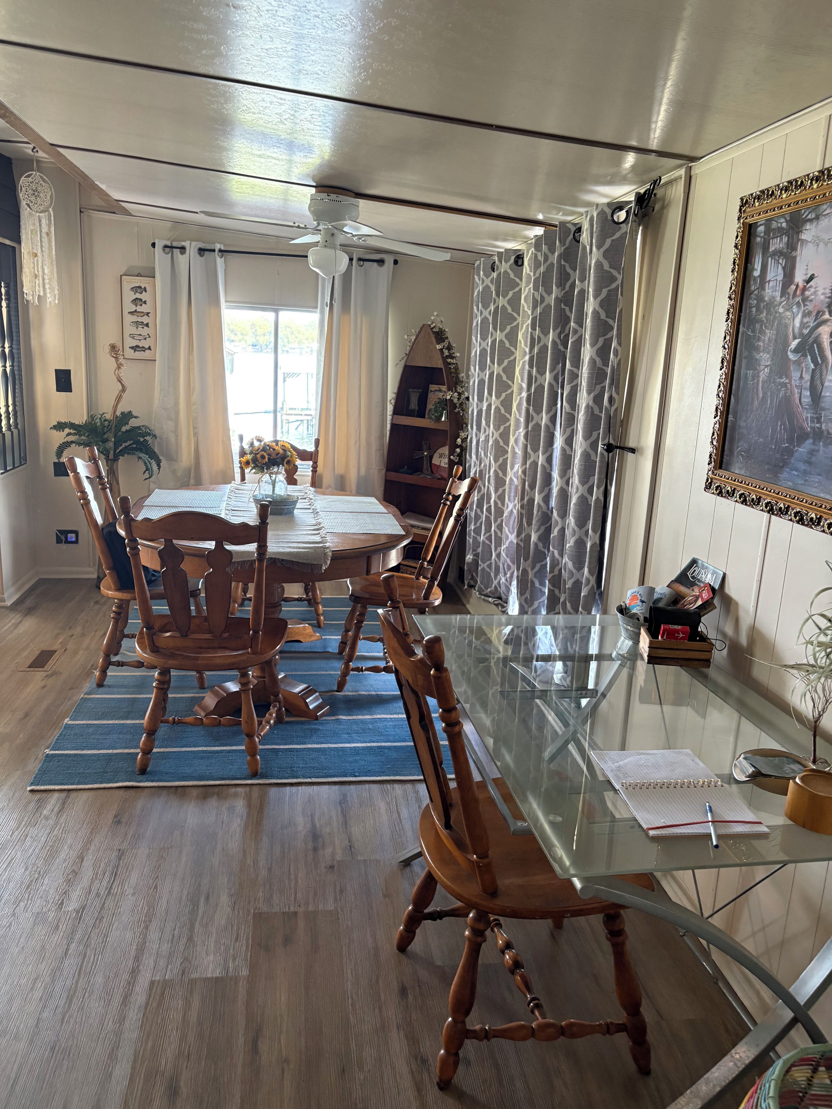 A dining area with a glass table, wooden chairs, a ceiling fan, and a view of the outdoors.