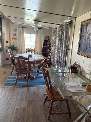 A dining area with a glass table, wooden chairs, a ceiling fan, and a view of the outdoors.