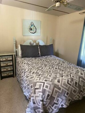 A bedroom with a bed, a nightstand, a wall-mounted artwork, and a ceiling fan.
